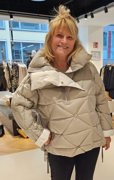 Frau in heller, gestepptem Winterjacke mit großer Kapuze in einem Geschäft.