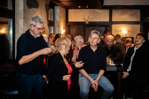 Gesellige Gruppe von Menschen in einem Pub, einige stehen, andere sitzen, lächeln und plaudern.