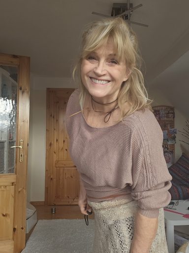 Lächelnde Frau mit blonden Haaren in einem gemütlichen Raum.