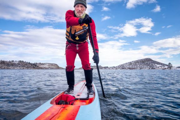 Ein Mann steht auf einem Stand-Up-Paddleboard und zeigt mit dem Finger.