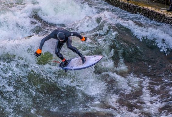 Surfer in schwarzem Anzug mit orangefarbenen Handschuhen reitet eine Welle.