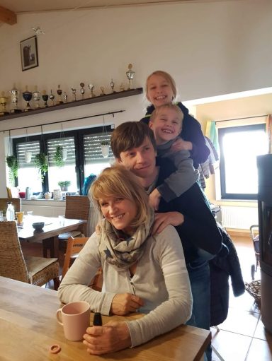 Familie sitzt zusammen; zwei Kinder sitzen auf den Schultern eines Erwachsenen.
