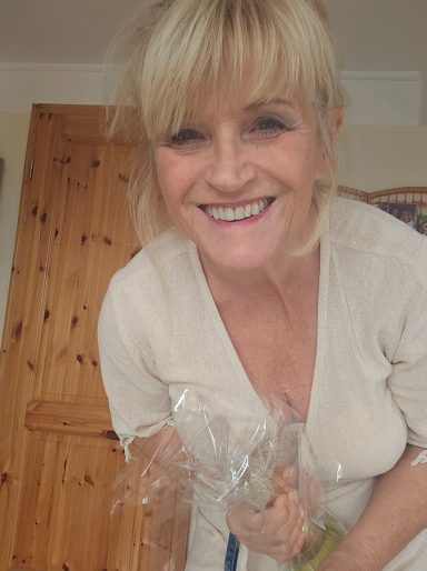 Lächelnde Frau mit blonden Haaren hält eine Tüte mit Pflanzen.