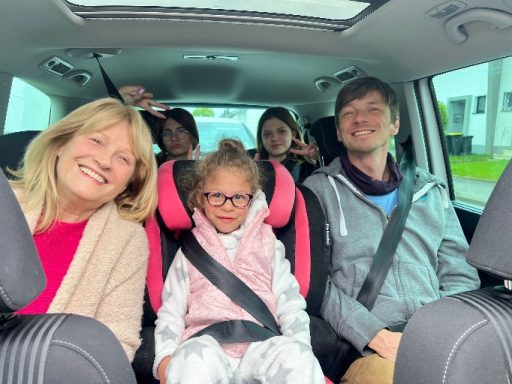 Fünf Personen sitzen im Auto, lächeln und posieren fröhlich für ein Foto.