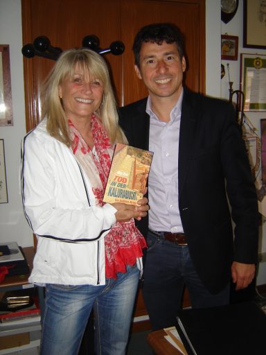 Zwei Personen stehen zusammen, eine mit einem Buch in der Hand, beide lächeln.